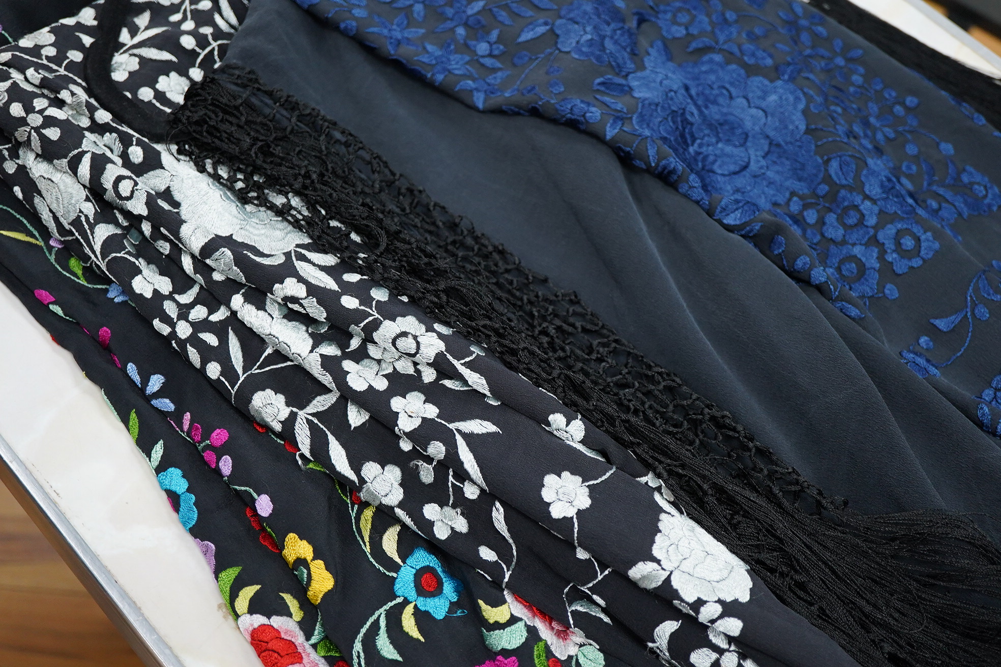 Three Chinese shawls, 1930’s machine floral embroidered, on black silk crepe de chine. One multicoloured, one navy blue, the other white embroidery. Largest navy and white shawls:130cm x 120cm. Condition - no stains, fad